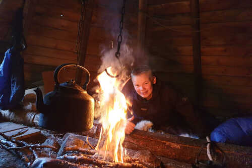 Boy sits by the fire in the lavvo.