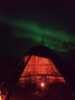 Lavvo with light inside and northern lights in the sky.