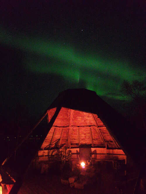 Lavvo med lys inni og nordlys på himmelen.